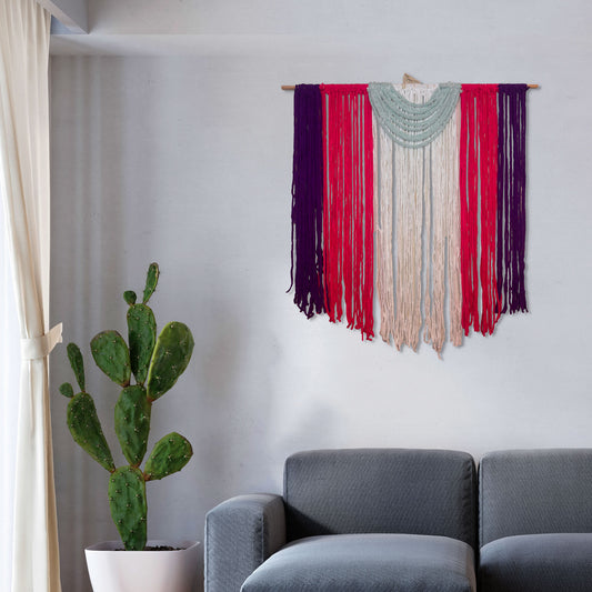 Medium handmade macramé wall hanging with vertical strands of purple, coral, ivory, and blush yarn, with a draped green semi-circle accent on top